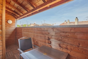 Een houten hutje met een tafel en stoel, een raam met uitzicht op een stadsgezicht.