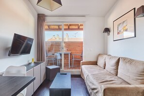 Een moderne kamer met een bank, een televisie, een eettafel en een balkon met uitzicht op gebouwen.