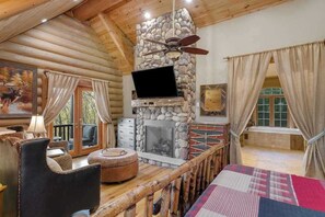 A log cabin interior with a stone fireplace, a television mounted on the wall, a wooden deck, and a cozy seating area. - Majestic Lodge Retreat (Morganton)