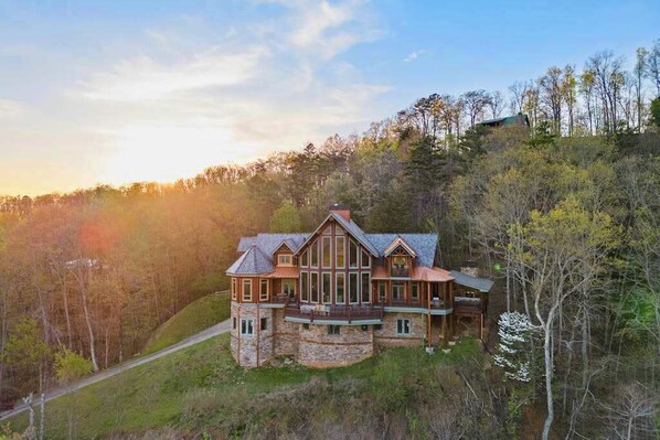 A large, multi-story stone house with a prominent balcony, surrounded by a forested hillside. - Majestic Lodge Retreat (Morganton)