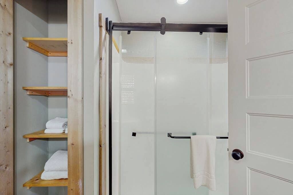 Un baño con cabina de ducha de vidrio, un perchero y estantes de madera con toallas.