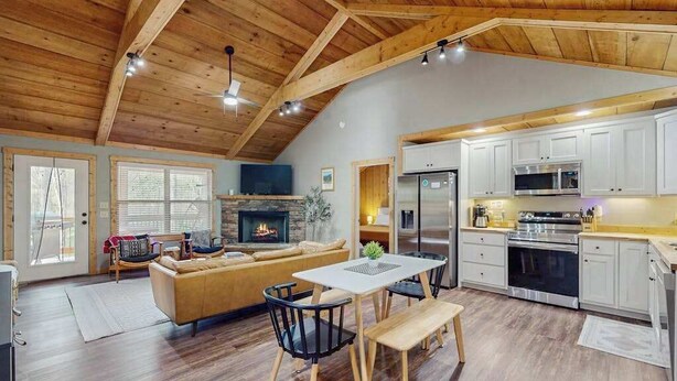 A spacious living area with a fireplace, a dining table with chairs, and a kitchen with white cabinets and modern appliances. - Dwell and Wander Stay (Ellijay)