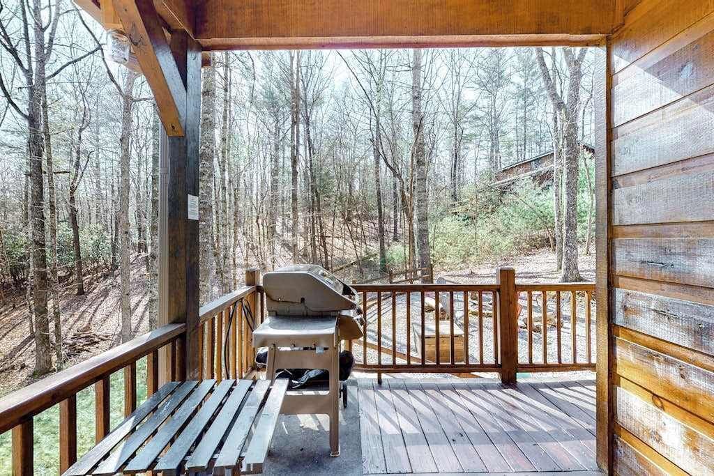 A wooden deck with a grill, a bench, and a view of a forest.