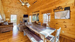Ein Holzblockhaus-Interieur mit Esstisch, Stühlen, einer Couch, einem Kamin und einer Karte an der Wand.
