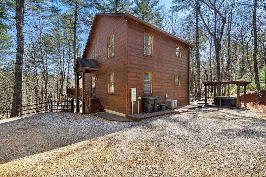 A wooden cabin with a porch, a covered outdoor seating area, and a gravel driveway.