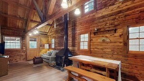 Interior de una cabaña de troncos con chimenea, bancos de madera y un sofá.