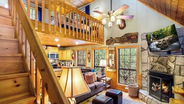 A wooden interior with a staircase, a fireplace, and a kitchen area. - Gunny's Cabin Retreat (Blue Ridge)