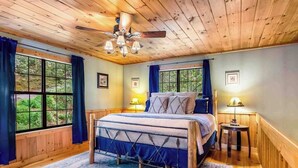 A bedroom with a bed, two bedside tables, a ceiling fan, and large windows. - Gunny's Cabin Retreat (Blue Ridge)