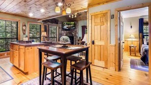 A wooden interior with a kitchen island, bar stools, a stone fireplace, and a view through large windows. - Gunny's Cabin Retreat (Blue Ridge)
