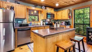 A kitchen with wooden cabinets, stainless steel appliances, and a large window. - Gunny's Cabin Retreat (Blue Ridge)