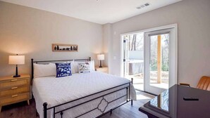 Un dormitorio con cama, mesitas de noche, un escritorio y un ventanal corredero al exterior.
