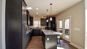 Una cocina moderna con armarios oscuros, una isla central, iluminación colgante y ventanas amplias.