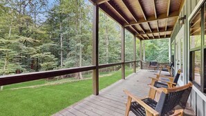 A covered porch with wooden chairs and a view of a forest. - The Hidden Haven Stay (Blue Ridge)