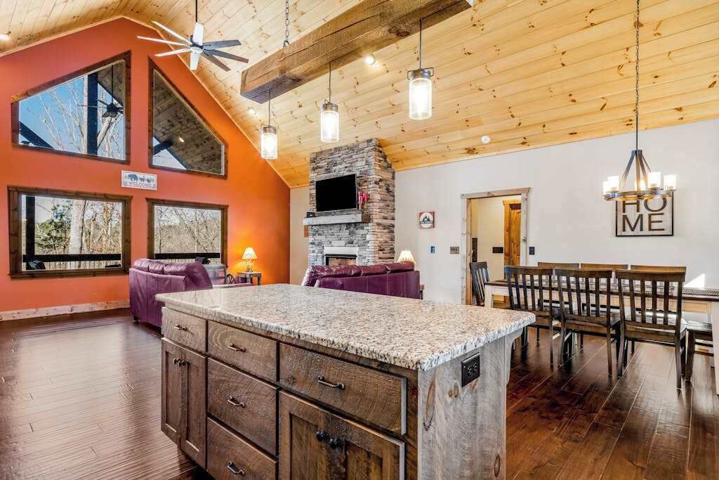 A spacious kitchen with a stone fireplace, wooden ceiling beams, and a dining area with a bench.
