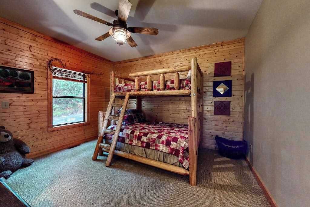 Habitación con literas, ventilador de techo, una ventana y un oso de peluche en el suelo.