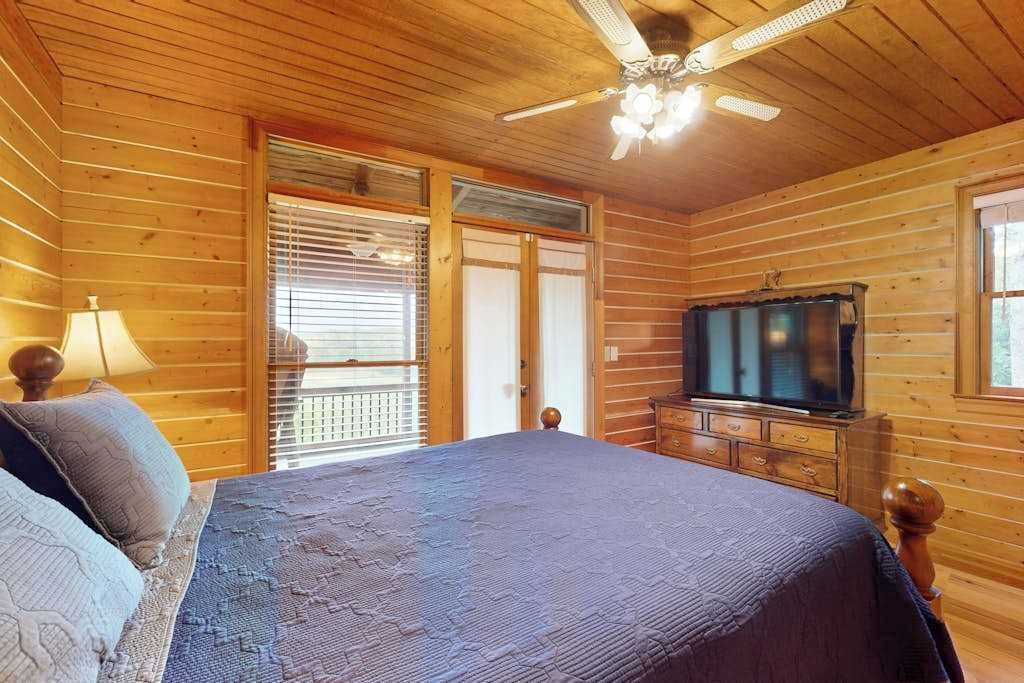 Une chambre dans une cabane en bois, équipée d’un lit, d’une télévision et d’un ventilateur de plafond.