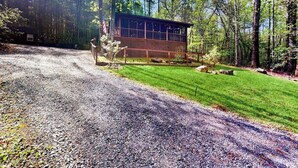 A cabin with a gravel driveway, surrounded by trees and a well-maintained lawn. - Bluebird Bliss Cabin (Blue Ridge)