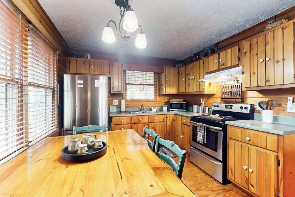 Une cuisine avec des meubles en bois, un réfrigérateur en acier inoxydable, une cuisinière et une table à manger avec des chaises.