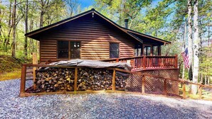 A log cabin with a porch, a stack of firewood, and an American flag. - Bluebird Bliss Cabin (Blue Ridge)