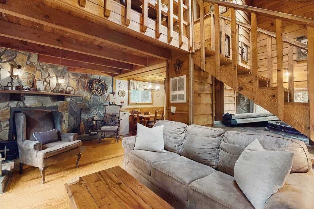 A wooden interior with a stone fireplace, a sofa, and a staircase.