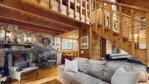A wooden interior with a stone fireplace, a sofa, and a staircase.
