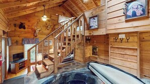 A wooden cabin interior with a hot tub, wooden staircase, and mounted animal heads.