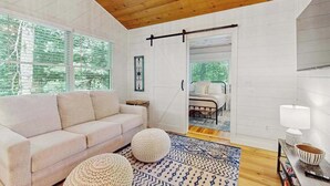 Ein modernes Interieur mit Holzbalkendecke, einer Couch, einem gemusterten Teppich und einem Bett im Hintergrund.