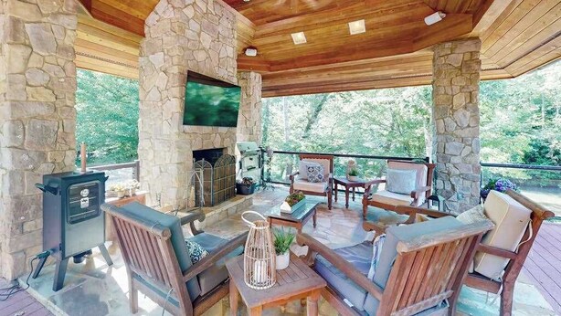 A covered outdoor seating area with stone pillars, a fireplace, and a flat-screen TV. - River Runs Through It (Dahlonega)