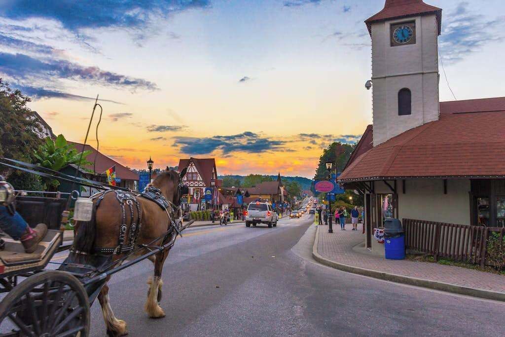 A horse-drawn carriage on a street with buildings, a clock tower, and a sunset.