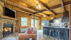 L’intérieur d’un chalet rustique, avec une cheminée en pierre, des poutres en bois, un canapé, un coin bar et une cuisine.