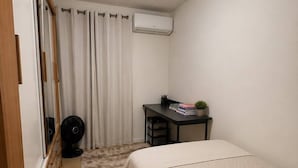 Et soveværelse med seng, skrivebord med stol, aircondition og ventilator.