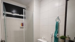 Et badeværelse med bruser, toilet, håndvask og et håndklæde hængende på væggen.