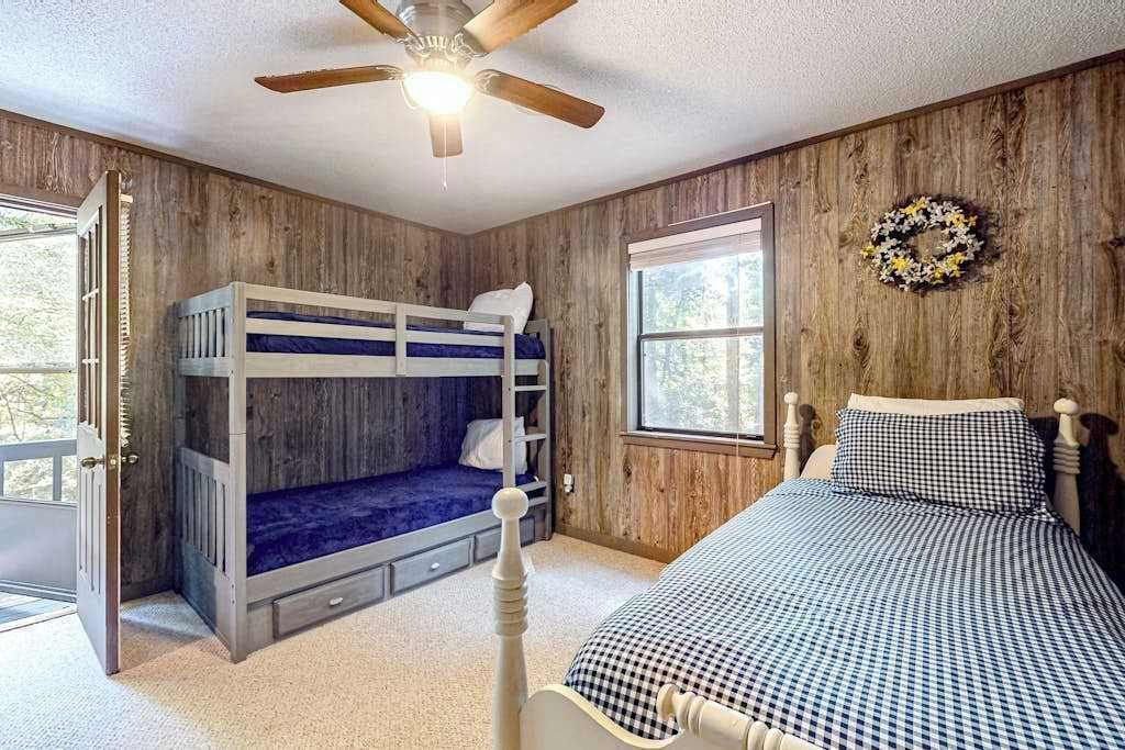 Een kamer met stapelbedden, een plafondventilator, een raam met een krans en een deur.