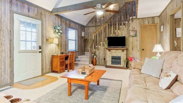 Een rustiek interieur met een open haard, houten wanden, een plafondventilator en een televisie.