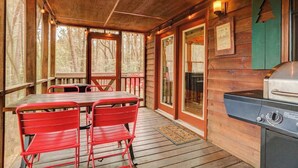 A wooden deck with a table and chairs, a grill, and framed certificates on the wall. - Bear in the Woods Stay (Blue Ridge)