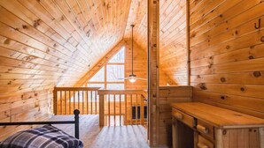 A wooden cabin interior with a loft bedroom, a wooden desk, and a window. - Bear in the Woods Stay (Blue Ridge)