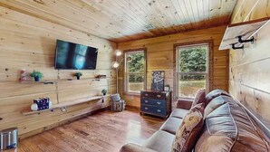 Een houten interieur met een televisie, bank en ramen.