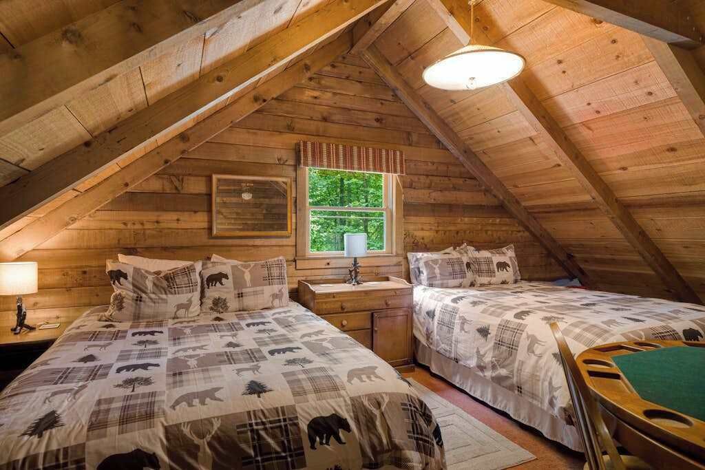 Ein gemütliches Schlafzimmer im Dachgeschoss mit zwei Betten, einem Fenster und einer Holzbalkendecke.