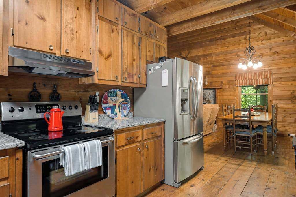 A wooden cabin kitchen with a stove, oven, refrigerator, and wooden cabinets.