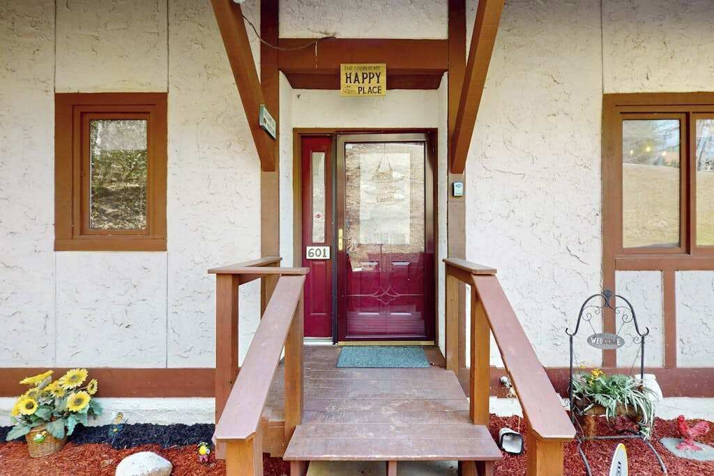 A wooden porch leading to a red door with a 'HAPPY PLACE' sign above, number 601, and a welcome sign beside it.