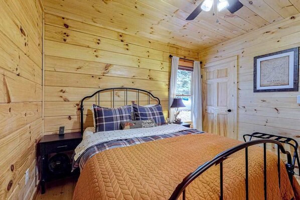 Une pièce de cabane en bois comprenant un lit, une table de chevet, une lampe et une porte.