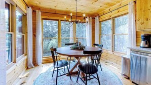 Un interior de madera con una mesa redonda, sillas, un candelabro y ventanas amplias.
