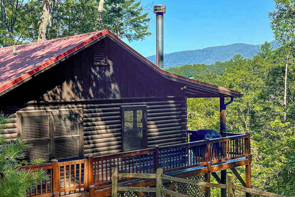 A log cabin with a metal roof, a chimney, and a wooden deck.