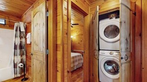 A wooden cabin interior with a washing machine, a bed, and a shower area. - Ogana Ridge Getaways (Ellijay)