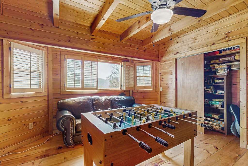 A wooden-floored room with a foosball table, a leather couch, and a bookshelf.