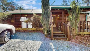 A log cabin with a wooden porch and steps, a vehicle parked in front, and a gravel driveway. - Wonderland Ellijay Stay (Ellijay)