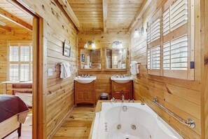 Une salle de bain rustique, avec une grande baignoire, deux lavabos et un miroir.