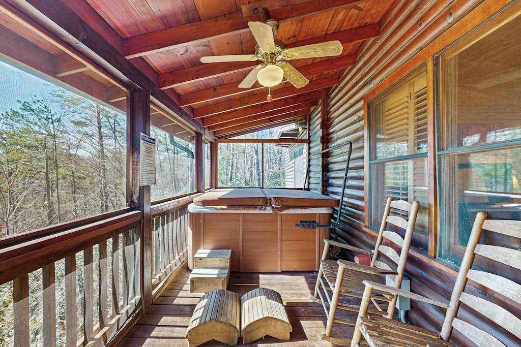 Une cabane en rondins avec une terrasse en bois, un ventilateur de plafond et une vue sur la forêt.