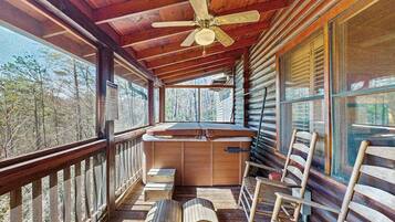 Une cabane en rondins avec une terrasse en bois, un ventilateur de plafond et une vue sur la forêt.