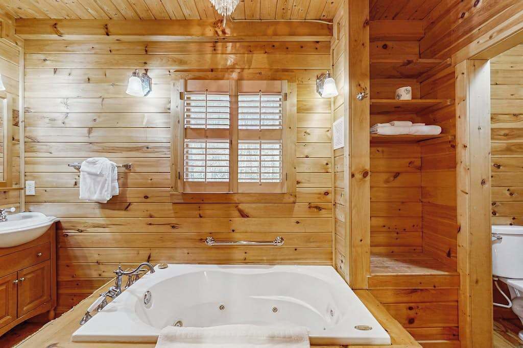 L’intérieur d’un chalet en bois, avec une grande baignoire, des murs en bois et une fenêtre avec des volets.